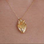 A gold anatomical heart pendant necklace worn on a person's neck, shown against light skin.