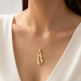 A gold necklace with a flame-shaped pendant worn by a model in a white V-neck top, shown in a close-up shot.